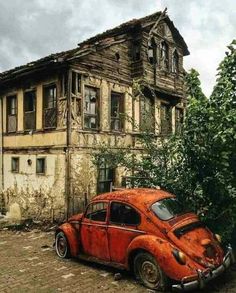 an old red car parked in front of a run down house