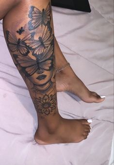 a woman's leg with butterflies and flowers on it, sitting on a bed