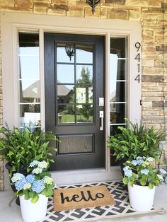 two potted plants are sitting on the front porch with a door mat that says hello