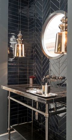 a black tiled bathroom with a sink and mirror on the wall, along with two hanging lights