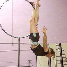 a woman doing aerial tricks on a hoop in a gym with pink walls behind her