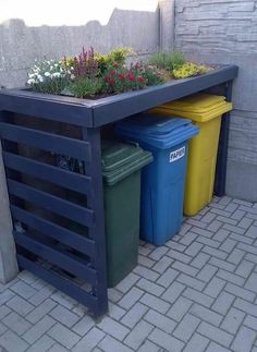 three trash cans are sitting next to each other on the side of a building with plants growing out of them