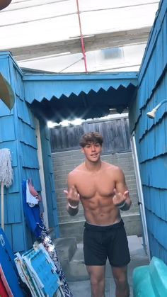 a man with no shirt standing in front of a blue shed holding his hands up