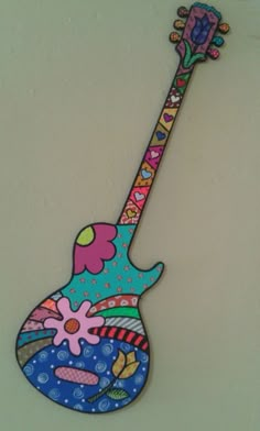 an image of a colorful guitar hanging on the wall with flowers and hearts painted on it