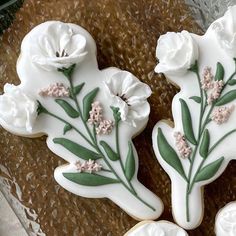 two decorated cookies sitting on top of a glass plate covered in frosting and flowers