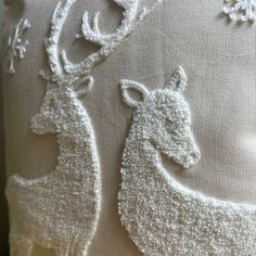 two deer embroidered onto the side of a white pillow with snow flakes on it