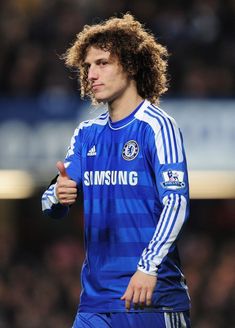 a young man with curly hair wearing a blue soccer uniform and giving the thumbs up