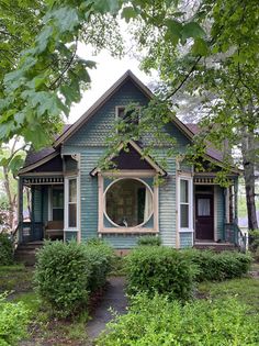 a small blue house with a round window in the front yard and bushes around it