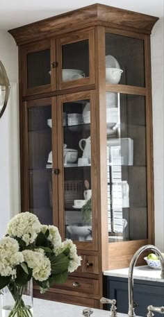 a wooden cabinet with glass doors and flowers in a vase on the sink countertop