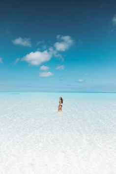 a woman standing in shallow water on top of a white sandy beach next to the ocean