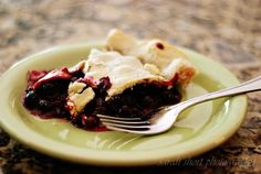 a piece of pie on a green plate with a fork in the foreground and a marble counter top behind it