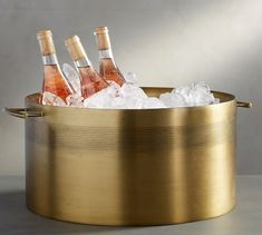 three bottles of wine in a gold ice bucket on a grey surface with ice cubes