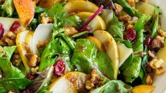 a salad with apples, walnuts and cranberries in a white bowl on a table