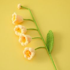 crocheted flowers are arranged on a yellow surface with green stems and leaves in the foreground