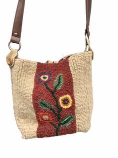 a small purse with flowers on the front and brown leather straps, sitting on a white surface