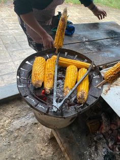 corn on the cob being grilled over an open fire pit with tongs