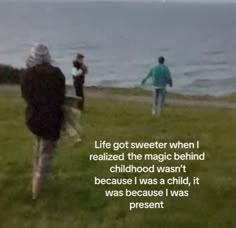 three people are walking in the grass by the water