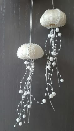 two white crocheted jellyfishs hanging from hooks on a wall with beads