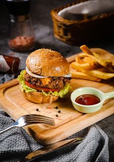 a chicken sandwich with lettuce and tomato on a cutting board next to french fries