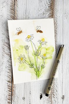 a watercolor painting of daisies and bees on a piece of paper next to a marker