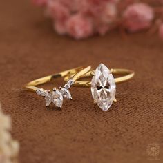 two diamond rings sitting on top of a brown surface next to pink flowers and petals