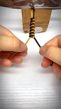 two hands holding a yellow and black string in front of a piece of metal foil