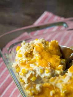 a spoon full of mashed potatoes and corn in a glass dish on a pink towel