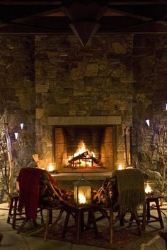 two chairs and a table in front of a fire place with candles on each side