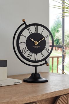 a black clock sitting on top of a wooden table next to a book and plant