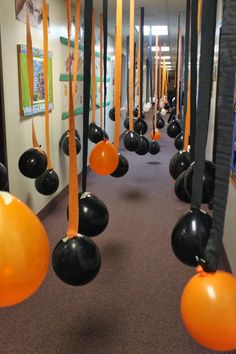 orange and black balloons are hanging from the ceiling in an office hallway that is decorated with art