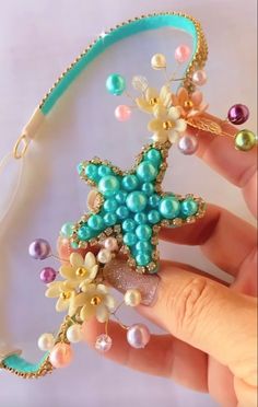 a hand holding a starfish brooch with pearls and beads on it's side