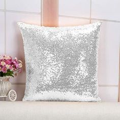 a silver sequin pillow sitting on top of a white bench next to a vase with flowers