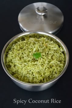 a metal bowl filled with green rice on top of a black table next to a saucer