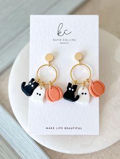 the cat and dog earrings are sitting on top of a white plate next to a card