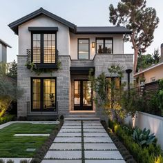 a modern home with stone and grass in the front yard at dusk, surrounded by greenery