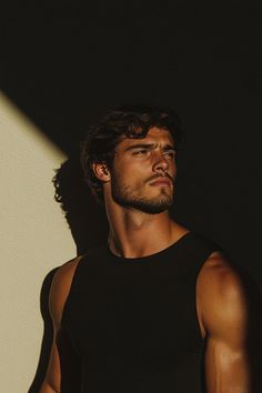 a man standing in front of a white wall wearing a black tank top and jeans