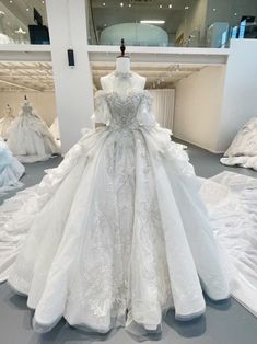 a white wedding dress on display in a room with other dresses and gowns behind it