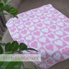 a pink and white crocheted blanket sitting next to a potted plant