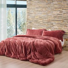 a large bed covered in a red comforter next to a brick wall and window