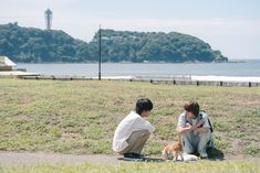 two people sitting on the ground with a dog in front of them and an island in the background