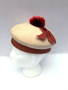 Adorable Rare Mr.John New York/ Paris Juniorette felt pom pom hat. Mr John's most famous work was his millinery for Vivien Leigh in Gone With The Wind. he had a long association with Hollywood and Broadway. He attributed all his success to Mary Pickford. Hat is ivory felt with rusty red colored raffia pom pom and apricot colored grosgrain ribbon. Some light spots on grosgrain ribbon as shown. Sold as-is.  This is a final sale. measurements inside circumference 19.5 FAQ:Terms and Info regarding i Vintage Beige Felt Hat For Winter, Vintage Red Hat For Fall, Vintage Winter Beret With Short Brim, Retro Winter Beret, Vintage Wool Beret For Winter, Madeline Aesthetic, Pom Pom Clothes, Felt Pom Pom, Fashion 1950