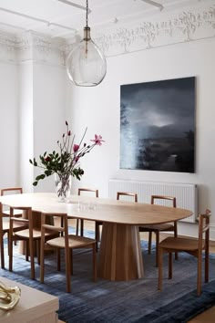 a dining room table with chairs and a vase filled with flowers on top of it