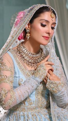 a woman in a blue and gold bridal gown with jewelry on her head, looking down