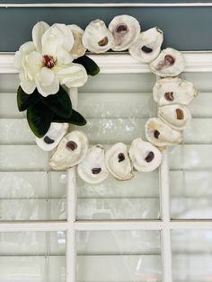 a wreath made out of seashells and flowers hangs on the window sill