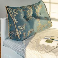 a blue pillow sitting on top of a white bed next to a book and lamp