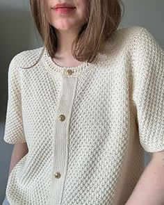 a woman wearing a white sweater standing in front of a wall with her hands on her hips