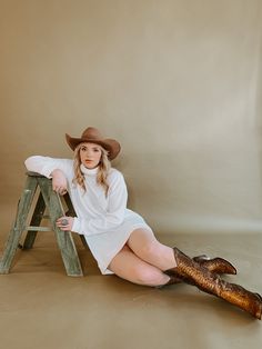 a woman sitting on top of a wooden step stool wearing a cowboy hat and boots