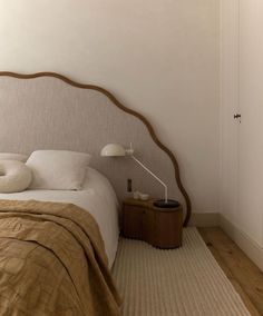 a bed with a headboard and pillows on it in a room that has white walls