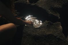 a person kneeling down in the dirt with their hand on a glass object that is glowing