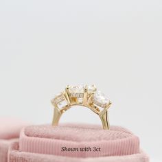 a three stone diamond ring sitting on top of a pink velvet bag